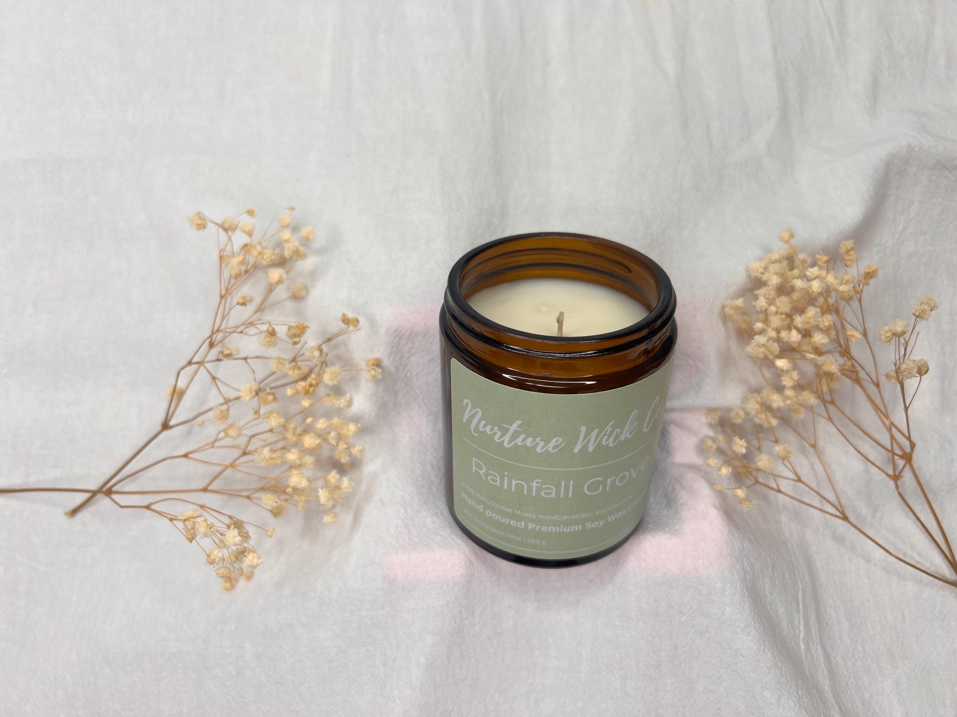 Candle in a glass jar with a label on a light gray background with dried flowers.