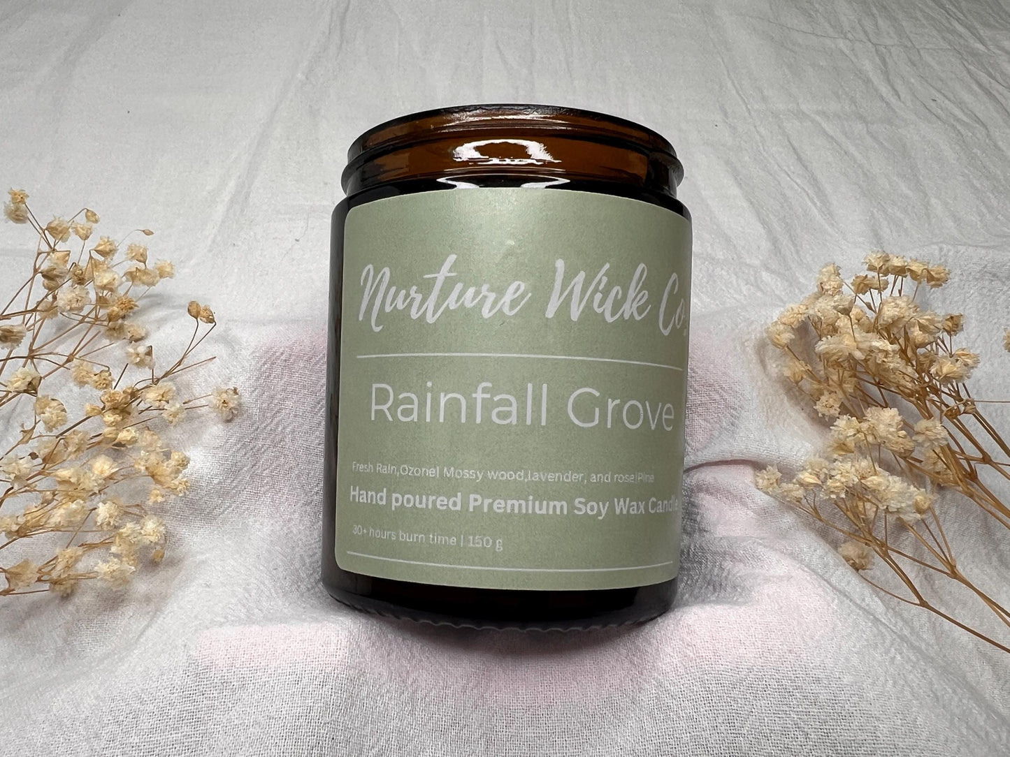 Candle with 'Nurture Wick' label on a textured surface with dried flowers