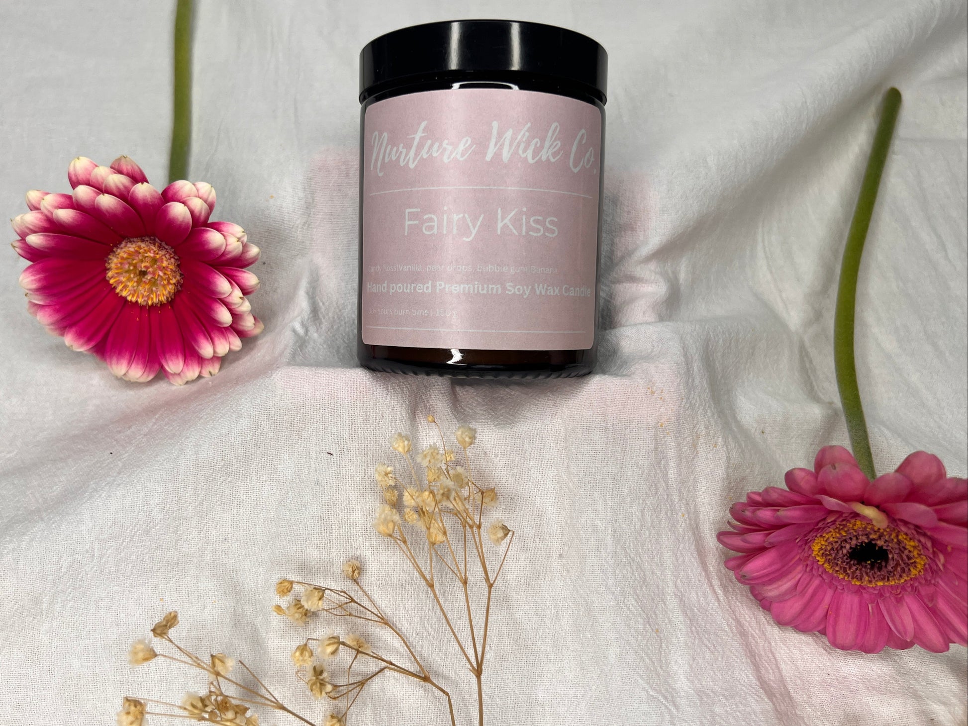 Jar of 'Fairy Kiss' product with pink flowers on a white fabric background