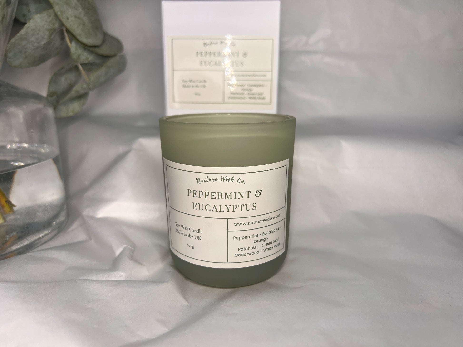 Candle labeled 'Peppermint & Eucalyptus' with a white box in the background on a light gray surface.