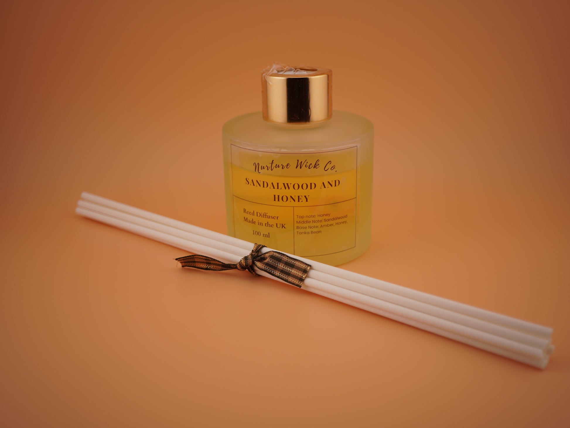 Sandalwood and honey diffuser with reeds on an orange background